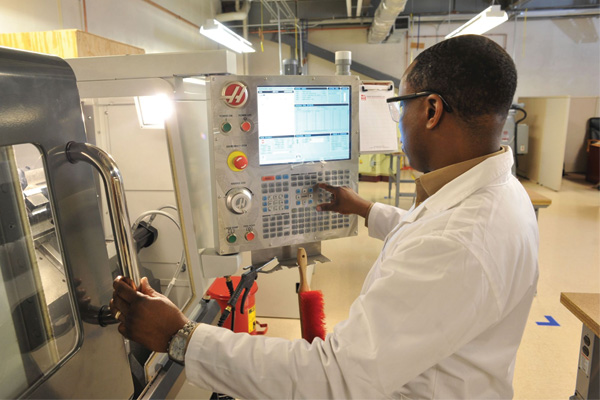 man in factory lab coat operating machine control panel stainless steel door